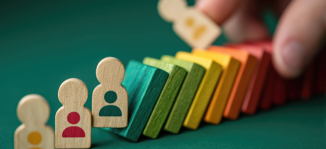 Domino effect of personnel changes. A hand topples a colorful domino line of miniature people figures