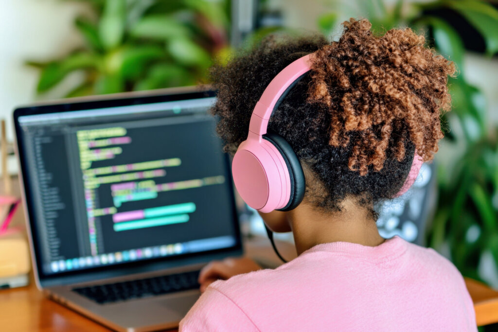 Teenage girl sits at laptop and coding. Black teen girl uses AI powered tool, interactive lessons. Online education, technology, artificial intelligence, science concept
