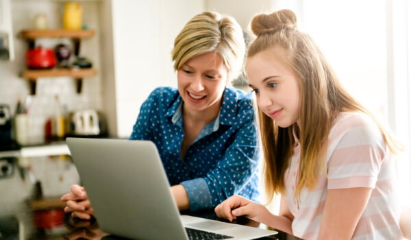 A mother using a laptop in kitchen with teenager