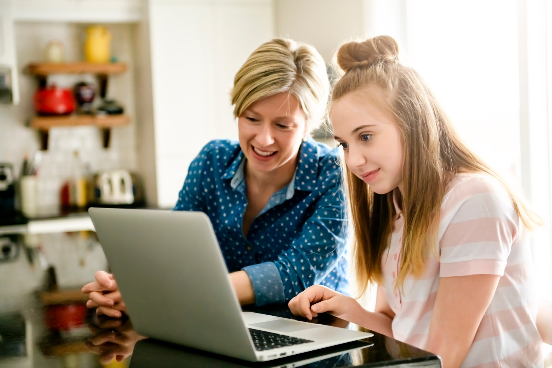 A mother using a laptop in kitchen with teenager